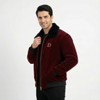 Angled front view of men's maroon velvet winter jacket with black faux fur collar, with the model holding the collar and smiling.