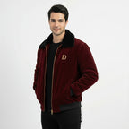 Angled front view of men's maroon velvet winter jacket with black faux fur collar, hands in pockets, worn over a black t-shirt.